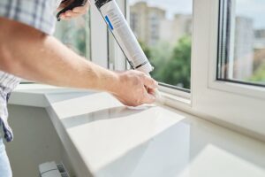 Worker with construction syringe fills seam between sill and window with silicone sealant