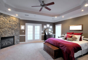 Interior of a large modern bedroom with a fireplace and ceiling fan.