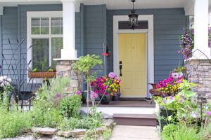 Yellow front door of a house. Attractive and colorful front porch surrounded by perennial and annual flowers in summer.